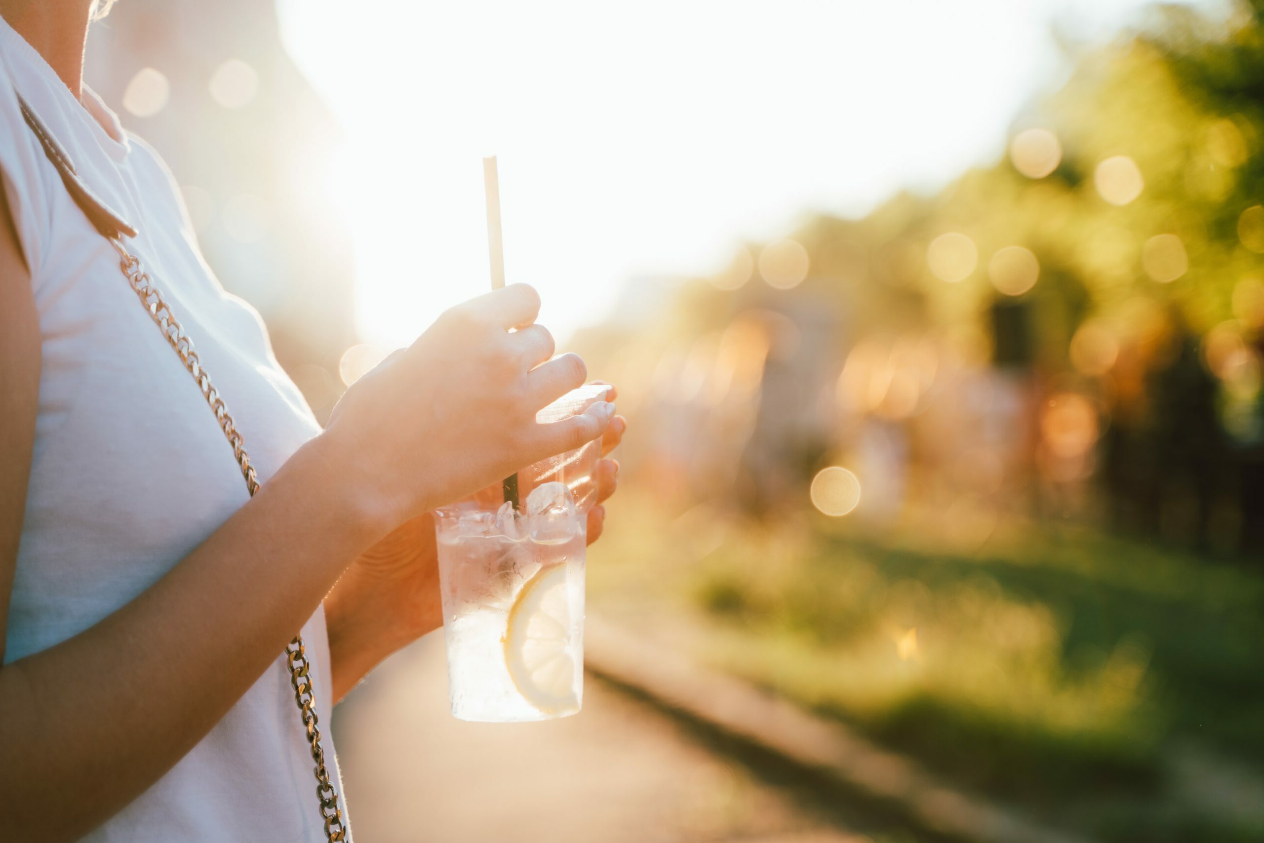 Person in white shirt enjoys a cold drink after visiting a med spa in Hayden Idaho, holding cup with straw, ice, and lemon outside. at North Idaho Med Spa in Hayden