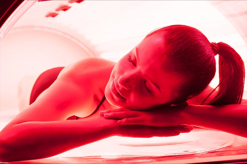 A woman relaxes in a red light tanning bed at a Hayden Idaho med spa, smiling with her head on folded arms for skin rejuvenation. at North Idaho Med Spa in Hayden