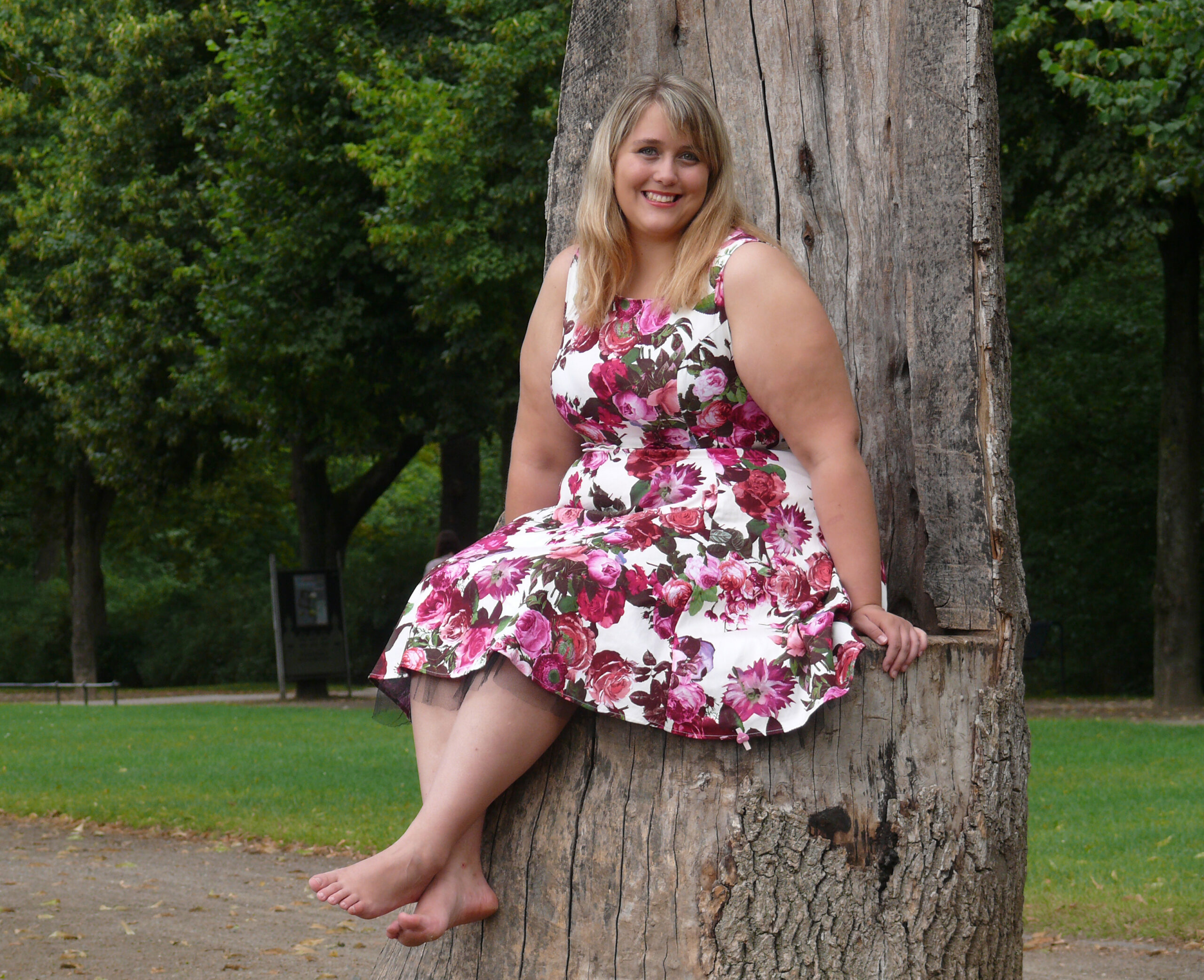 A relaxed woman in a floral dress sits barefoot on a tree stump in a lush park, reflecting serenity found at Hayden Idaho Med Spa. at North Idaho Med Spa in Hayden