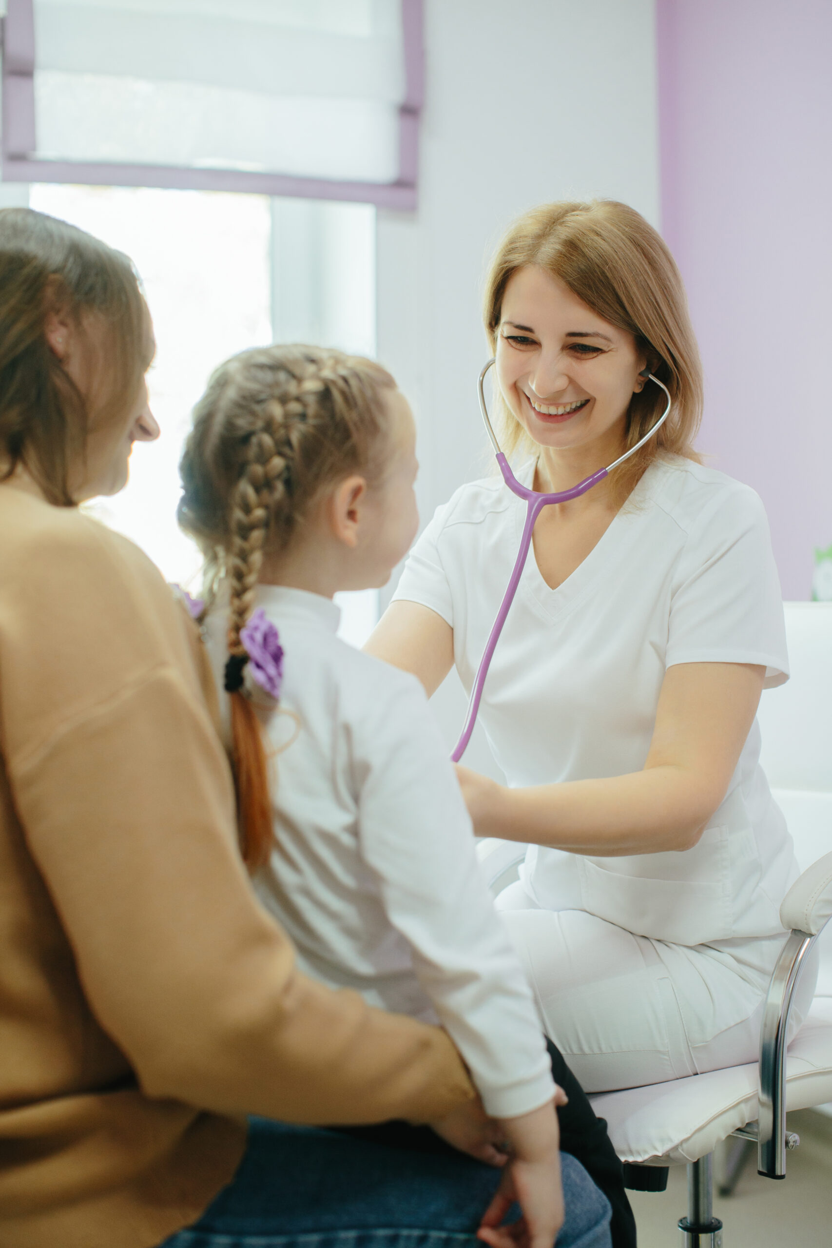 a healthcare provider in a hayden, idaho med spa checks a young girl's heartbeat with a stethoscope as she sits on an adult’s lap. at north idaho med spa in hayden
