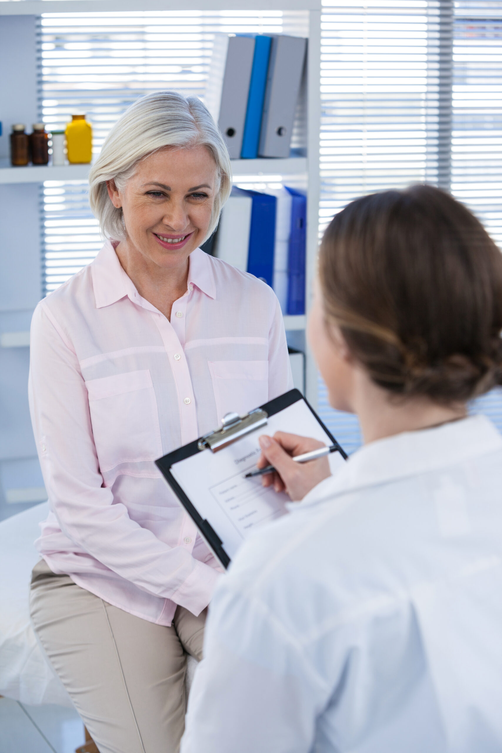 a woman smiles during a med spa consultation in hayden, idaho, as a professional in a white coat reviews notes on a clipboard. at north idaho med spa in hayden