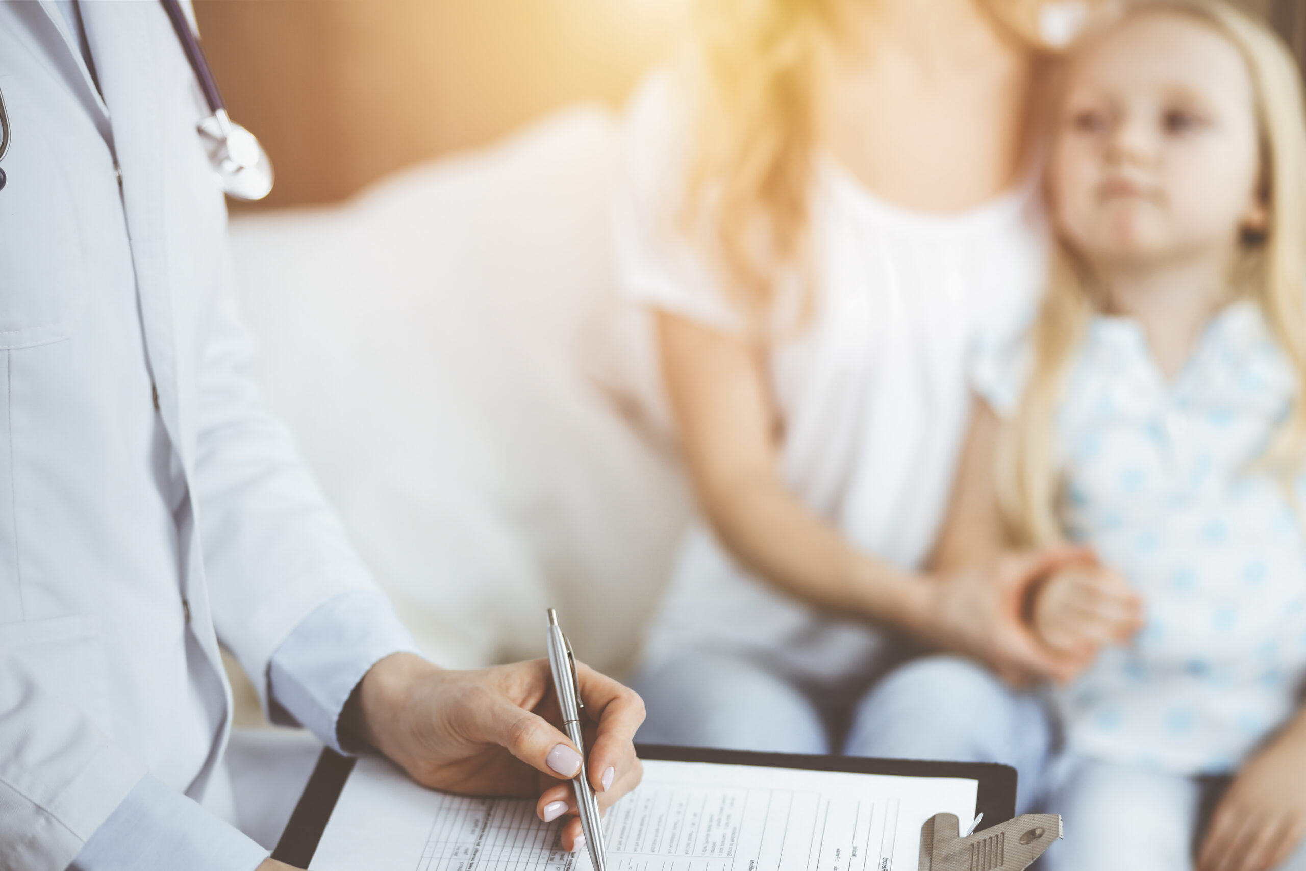 a doctor at a hayden idaho med spa fills out a medical form on a clipboard as a woman and young girl sit together nearby. at north idaho med spa in hayden